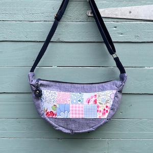 May include: A blue and grey patchwork fabric crossbody bag with a floral print. The bag has a long adjustable strap and a zip closure.