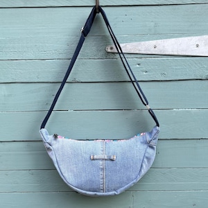 May include: A light blue denim crossbody bag with a black adjustable strap. The bag has a flap closure and a small pocket on the front.