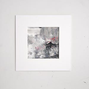 Può includere: Dipinto astratto in un passe-partout bianco. L'opera presenta una miscela di pennellate grigie, nere e bianche con accenti rossi. Il dipinto quadrato è montato in un passe-partout bianco, creando un'estetica pulita e moderna.