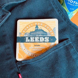 May include: A brown and yellow pocket pub guide for Leeds, England. The guide includes local independent breweries and features a vintage design with a city skyline illustration.