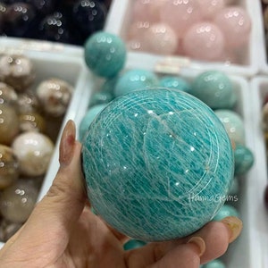 Pode incluir: Uma grande esfera de amazonita polida, de cor verde com um padr&atilde;o branco em espiral. A esfera est&aacute; sendo segurada em uma m&atilde;o.
