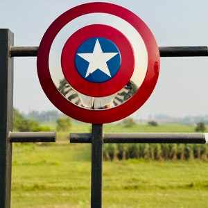 Detailed handmade shield with red, white, and blue design and a central star. Hero-inspired shield prop for cosplay, display, or gifts. Round patriotic shield designed for fans of classic comic book heroes. Metallic shield featuring a central star and layered circular design. Fantasy cosplay shield with retro comic-style finish.
