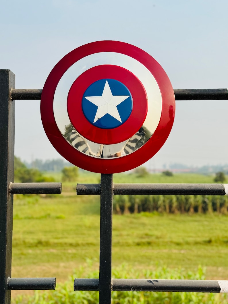 Detailed handmade shield with red, white, and blue design and a central star. Hero-inspired shield prop for cosplay, display, or gifts. Round patriotic shield designed for fans of classic comic book heroes. Metallic shield featuring a central star and layered circular design. Fantasy cosplay shield with retro comic-style finish.