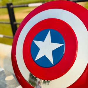May include: A red, white, and blue Captain America shield with a white star on a blue circle. The shield is made of metal and has a shiny finish.