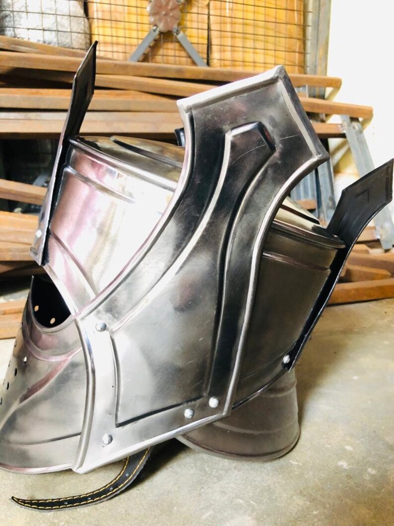 K&ouml;nnte beinhalten: Ein silberner Helm mit einer spitzen Spitze und einer Gesichtsmaske. Der Helm hat einen Lederriemen an der Unterseite.