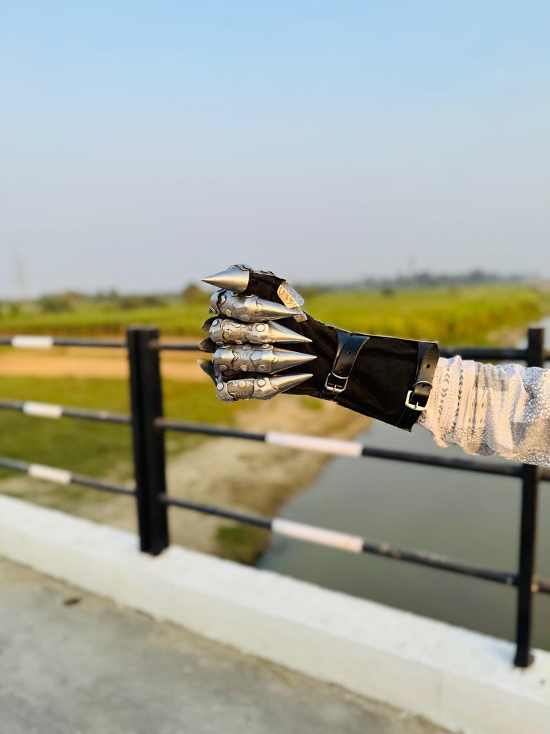 May include: A silver metal hand with pointed knuckles, worn as a glove, with a black leather wrist strap and buckle. The hand is clenched into a fist.