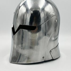 Puede incluir: Un casco medieval pulido de color plateado, con una parte superior redondeada y una abertura para la visera. El casco est&aacute; hecho de metal y tiene una superficie lisa y reflectante. Est&aacute; dise&ntilde;ado para proteger la cabeza y la cara.