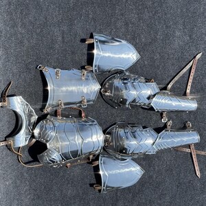 K&ouml;nnte beinhalten: Ein Satz polierter Silberr&uuml;stung, bestehend aus Brustpanzer, Schulterplatten und Armschienen. Die R&uuml;stung ist aus Metall und hat eine gl&auml;nzende Oberfl&auml;che.