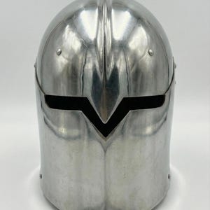 Puede incluir: Un casco pulido de color plateado con una distintiva visera en forma de V. El casco tiene una parte superior redondeada y est&aacute; construido con una sola pieza de metal. Los remaches aseguran la visera y la estructura del casco. El dise&ntilde;o sugiere un tema medieval o de fantas&iacute;a.