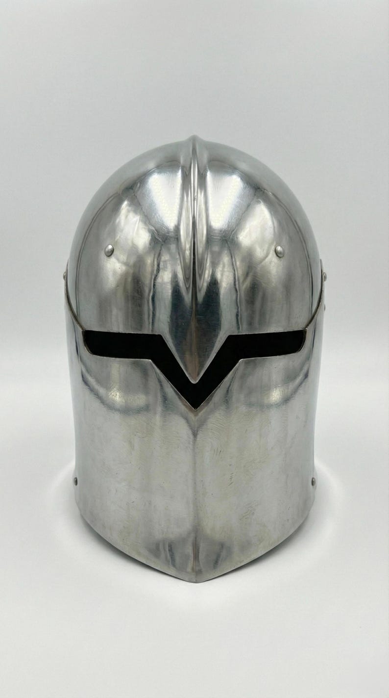 Puede incluir: Un casco pulido de color plateado con una distintiva visera en forma de V. El casco tiene una parte superior redondeada y est&aacute; construido con una sola pieza de metal. Los remaches aseguran la visera y la estructura del casco. El dise&ntilde;o sugiere un tema medieval o de fantas&iacute;a.