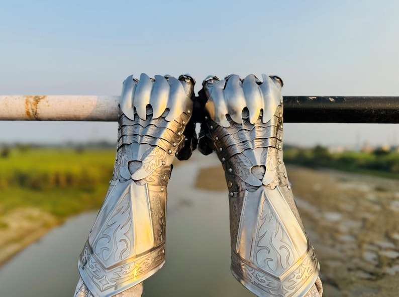 May include: A pair of silver metal gauntlets with intricate designs and pointed knuckles. The gauntlets are worn and have a rustic look.