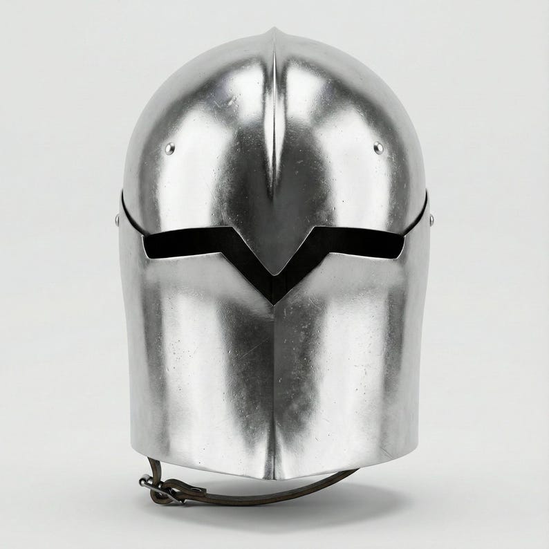 Puede incluir: Un casco plateado pulido con la parte superior redondeada y una abertura para la visera. El casco tiene una superficie lisa y reflectante y una correa para la barbilla. El dise&ntilde;o recuerda a la armadura medieval.