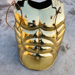 May include: A gold-coloured, muscular-style, Roman-style,  armour chest piece with leather straps.