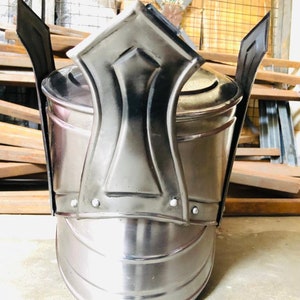 K&ouml;nnte beinhalten: Ein silberner Helm mit einer spitzen Oberseite und einem dekorativen Design. Der Helm hat eine abgerundete Basis und eine glatte, polierte Oberfl&auml;che.