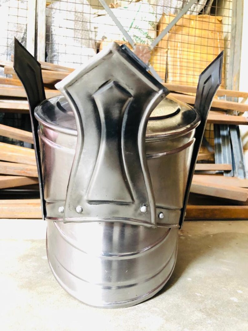 K&ouml;nnte beinhalten: Ein silberner Helm mit einer spitzen Oberseite und einem dekorativen Design. Der Helm hat eine abgerundete Basis und eine glatte, polierte Oberfl&auml;che.