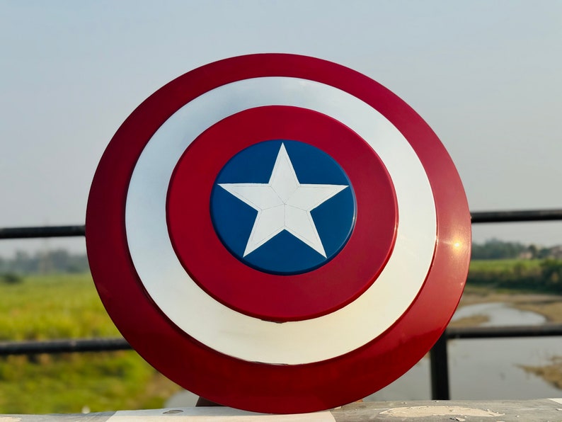 A Captain America shield replica.  The shield is round with concentric circles of red and white. A blue star with a white center is at the shield's center. The shield is made of a glossy material, possibly plastic or resin, and shows a high level of detail in its paint job. The colors are vibrant, and the design is clean and crisp. This is a collectible item for fans of Marvel comics and the Captain America character.