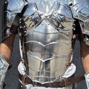 K&ouml;nnte beinhalten: Eine silberne Metallbrustplatte mit einem dekorativen Design. Die Brustplatte hat eine glatte, polierte Oberfl&auml;che und ist mit Riemen befestigt.