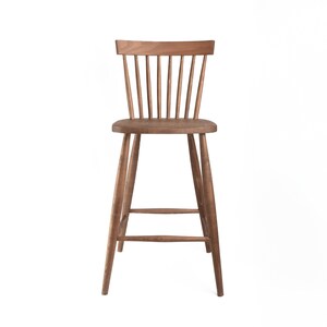 K&ouml;nnte beinhalten: Ein Barhocker aus Holz mit brauner Oberfl&auml;che und einer Lattenr&uuml;cklehne. Der Hocker hat ein schlichtes Design mit vier Beinen und einer Fu&szlig;st&uuml;tze.