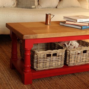 May include: A red wooden coffee table with a natural wood top. The table has two shelves, each with a woven wicker basket. The table is sitting on a red rug.