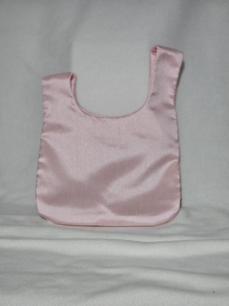 May include: A light pink satin tote bag with a rounded bottom and a single handle. The bag is made of a smooth, shiny fabric and is displayed against a white background.