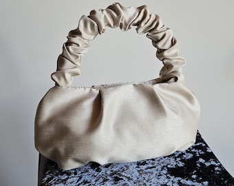 Peut inclure: Un sac à main en tissu beige plissé avec une anse en tissu plissé.