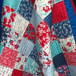 May include: A patchwork quilt with floral and geometric patterns in red, white, blue, and teal. The quilt is made of squares and diamond shapes, with a blue border. The quilt is a mix of patterns.