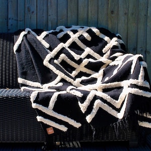 Könnte beinhalten: Schwarz-weiße Wolldecke mit geometrischem Muster. Die Decke ist aus weichem, strukturiertem Stoff und hat einen Fransenrand.