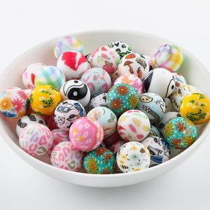 May include: A bowl filled with colourful round beads. The beads are made of plastic and have various patterns, including flowers, geometric shapes, and animals.