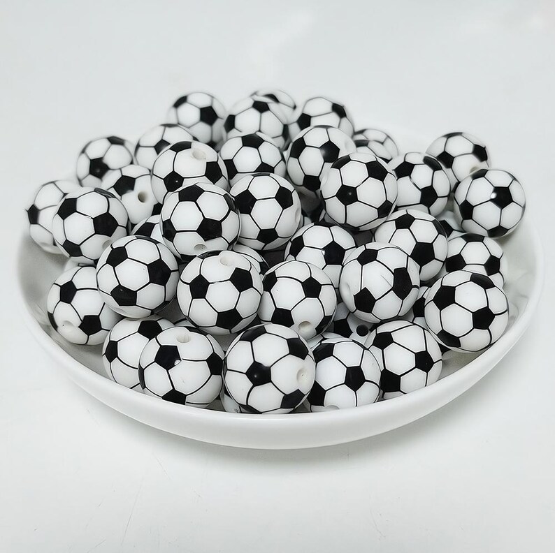 May include: A bowl filled with black and white football-shaped beads. The beads are made of plastic and have a glossy finish.