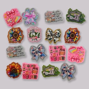 Pode incluir: Uma coleção de amuletos decorativos com vários designs. Inclui uma concha rosa com estrelas, uma pegada com um laço rosa e amuletos com texto como "Coffee Makes Me Nicer" e "Crazy Plant Lady".