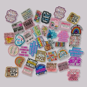 Può includere: Una collezione di spille smaltate colorate e glitterate con varie frasi e disegni umoristici. Le spille presentano testi come "Snarky", "Suspect" e "Easily Distracted by Dogs", insieme a immagini di arcobaleni, bucato e altro. Queste spille sono perfette per aggiungere personalità a borse, giacche o cordini.