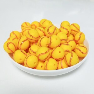 May include: A bowl filled with yellow silicone beads with red stitching, resembling baseballs.