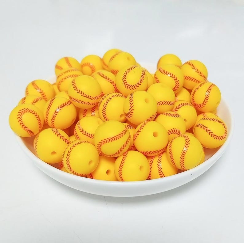 May include: A bowl filled with yellow silicone beads with red stitching, resembling baseballs.