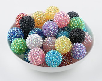 May include: A collection of colourful, sparkly, round beads. The beads are made of plastic and have a variety of colours, including pink, blue, green, yellow, and black.