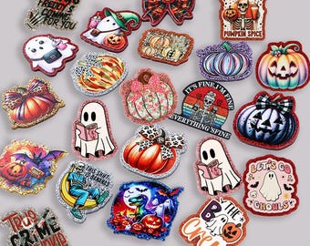 Puede incluir: Una colección de dijes acrílicos brillantes con temática de Halloween que incluyen fantasmas, calabazas, esqueletos y diseños de texto como One Two Freddy's Coming For You, My Blood Type Is Pumpkin Spice y True Crime Junkie.