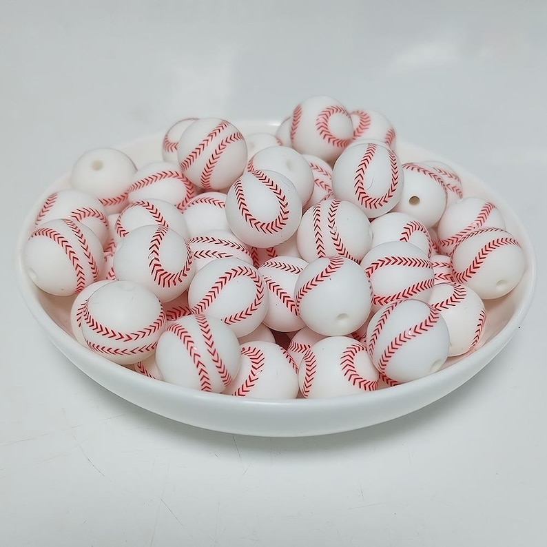 May include: A bowl filled with white silicone beads with red baseball stitching.