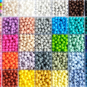 Könnte beinhalten: Eine Sammlung von Silikonperlen in verschiedenen Farben und Größen, angeordnet in einem Raster. Die Perlen sind in Reihen und Spalten angeordnet, wobei jede Reihe eine andere Farbe enthält. Die Perlen sind alle rund und haben eine glatte, matte Oberfläche.