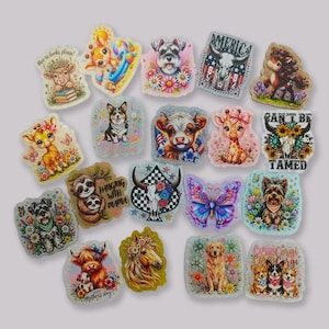 Puede incluir: Una colección de veinte pegatinas variadas con ilustraciones coloridas de animales como vacas, jirafas, perros, perezosos y caballos, junto a motivos florales, mariposas y calaveras con textos como 'More books, please!', 'Hanging with mama', 'America', 'Can't be tamed' y 'Corgi Corgi Corgi'.