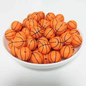 May include: A bowl filled with orange and black basketball-themed silicone beads. The beads are designed to look like basketballs with black lines.