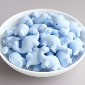 May include: A bowl filled with light blue dinosaur-shaped silicone beads.