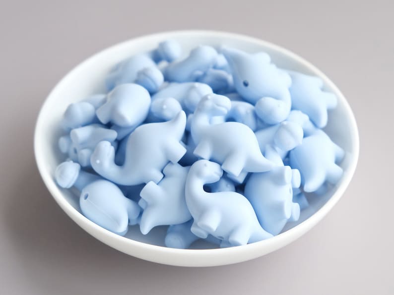 May include: A bowl filled with light blue dinosaur-shaped silicone beads.