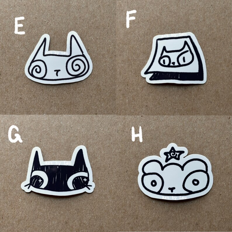 May include: Four black and white stickers featuring different animal designs. The stickers are on a brown surface. The designs include a cat with swirls, a cat wearing a hat, a cat with a black and white face, and a panda with a star.