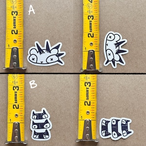 May include: Four black and white stickers with cartoon animal designs. The stickers are on a brown surface with a measuring tape on either side. The stickers are labeled A and B.