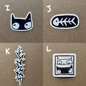 May include: Four black and white stickers on a brown background. The stickers are of a cat, a fish skeleton, a plant, and a cat in a frame. The text "Art by Leu" is on the fish skeleton and cat in a frame stickers.