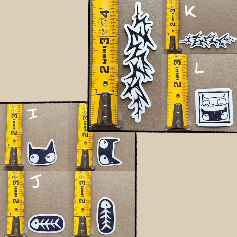May include: A set of nine black and white stickers featuring various designs, including a cat, a fishbone, and a stylized tree. The stickers are arranged on a brown surface with a yellow measuring tape.