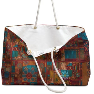 Pode incluir: Bolsa tote grande com um design de patchwork colorido com flores e um rosto sorridente. Possui alças de corda branca e interior branco. A bolsa está aberta, revelando o interior.
