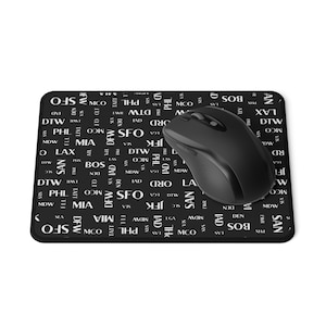 Könnte beinhalten: Eine schwarze Mausmatte mit einem sich wiederholenden Muster aus Flughafencodes in weißer Schrift. Die Mausmatte liegt auf einer weißen Oberfläche und eine schwarze kabellose Maus befindet sich auf der Mausmatte.