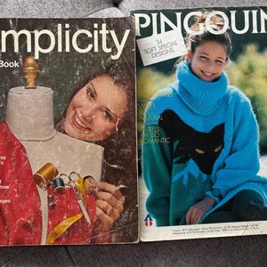 Könnte beinhalten: Zwei Vintage-Magazine. Das erste, "Simplicity Sewing Book", zeigt eine Frau und eine Schaufensterpuppe. Das zweite, "Pingouin", zeigt eine Frau in einem blauen Pullover mit einem schwarzen Katzenmuster. Beide Magazine haben Text.