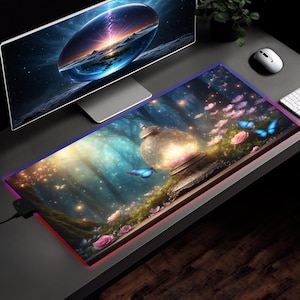 Peut inclure: Un tapis de souris lumineux bleu et violet avec une scène de forêt fantastique. La scène présente un orbe de verre lumineux, des papillons et des fleurs.