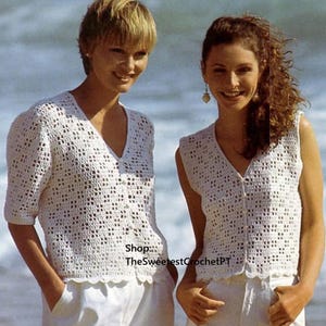 May include: Two women wearing white crochet tops with a V-neck design and button closures. The tops have a scalloped hemline. One top has short sleeves, and the other is sleeveless. Both are paired with white pants. The background is a beach scene.